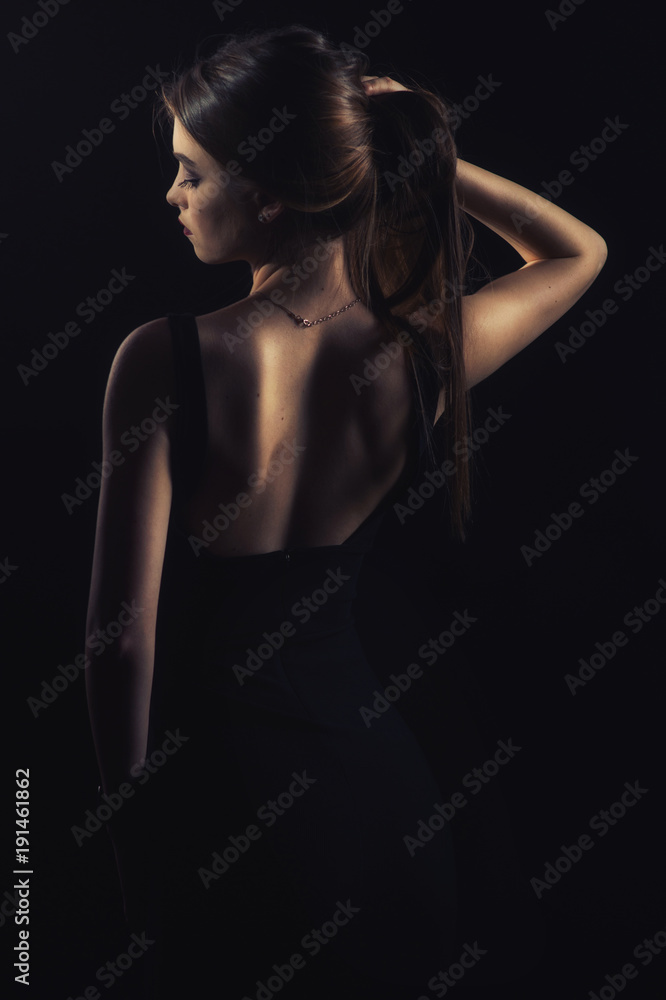 slim slim girl in dress with neckline in glamorous light from back slim slim girl in dress with neckline in glamorous light from back
