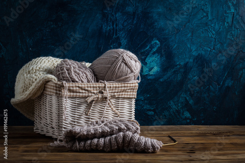 Light gray Knits in a basket and knitting needles, a white knitted scarf on a dark blue background. The concept of handmade