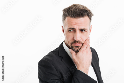 Photo of attractive businessman in suit looking aside with brooding look and touching his chin, isolated over white background © Drobot Dean