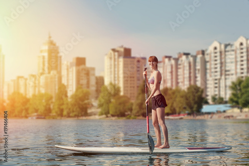 Young beautiful woman meditating on a river at SUP paddleboarding  in the city