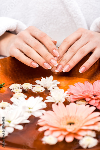 cropped view of woman making spa procedure with flowers, nail care concept