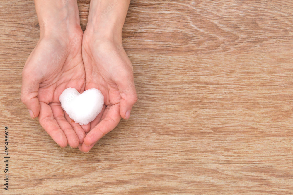 Snow heart in the woman's hands on the wooden table Snow heart in the woman's hands on the wooden table