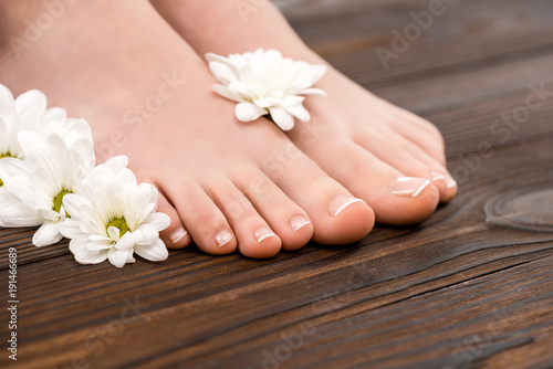 cropped view of feet with natural pedicure and flowers on wooden surface