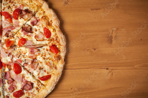Fresh Italian pizza with ham, cherry tomatoes and parmesan on wooden table. Top view, place for text.