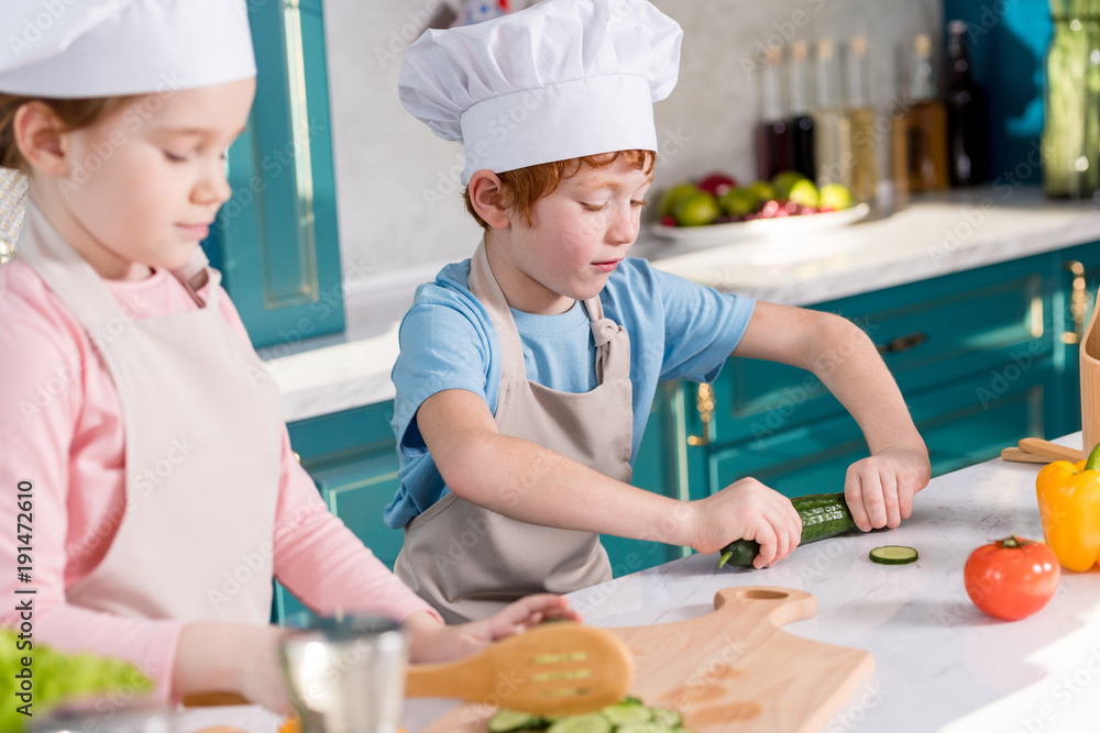 children in chef hats and aprons preparing vegetable salad together in kitchen children in chef hats and aprons preparing vegetable salad together in kitchen