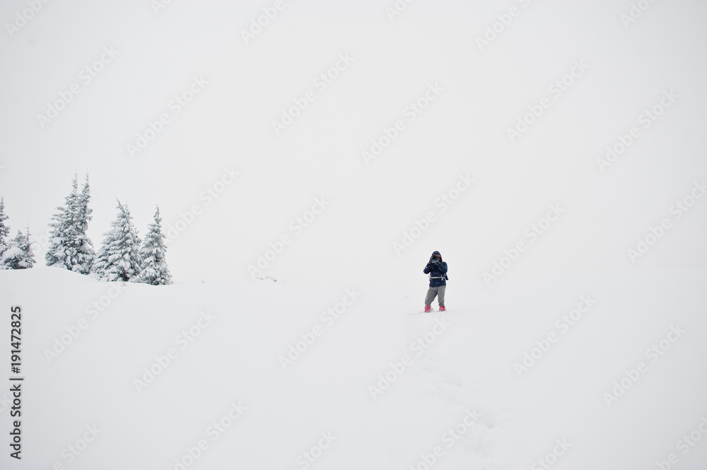 Man tourist photographer with backpack, at mountain with pine trees covered by snow. Beautiful winter landscapes. Frost nature.