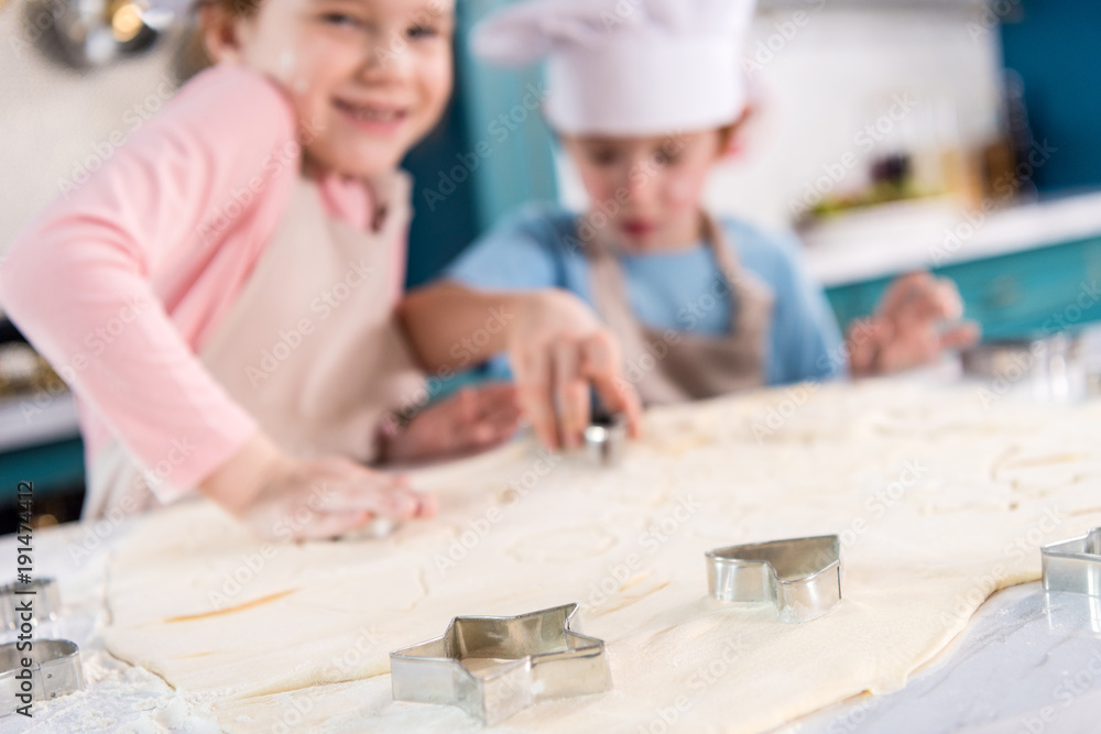 close-up view of uncooked dough and forms for cookies and cute little children in kitchen close-up view of uncooked dough and forms for cookies and cute little children in kitchen