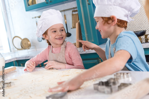 cute little children smiling each other while preparing cookies together