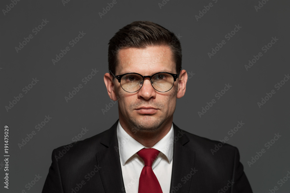 An angry businessman in formal suit and glasses looks at the camera on gray background An angry businessman in formal suit and glasses looks at the camera on gray background