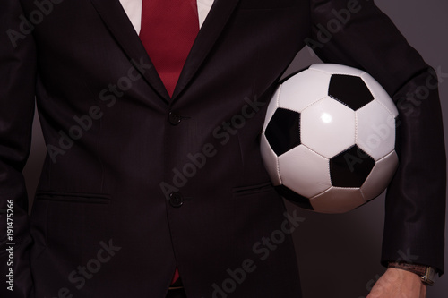 Fototapeta Naklejka Na Ścianę i Meble -  Close-up - businessman in formal suit holds football ball in his hands.