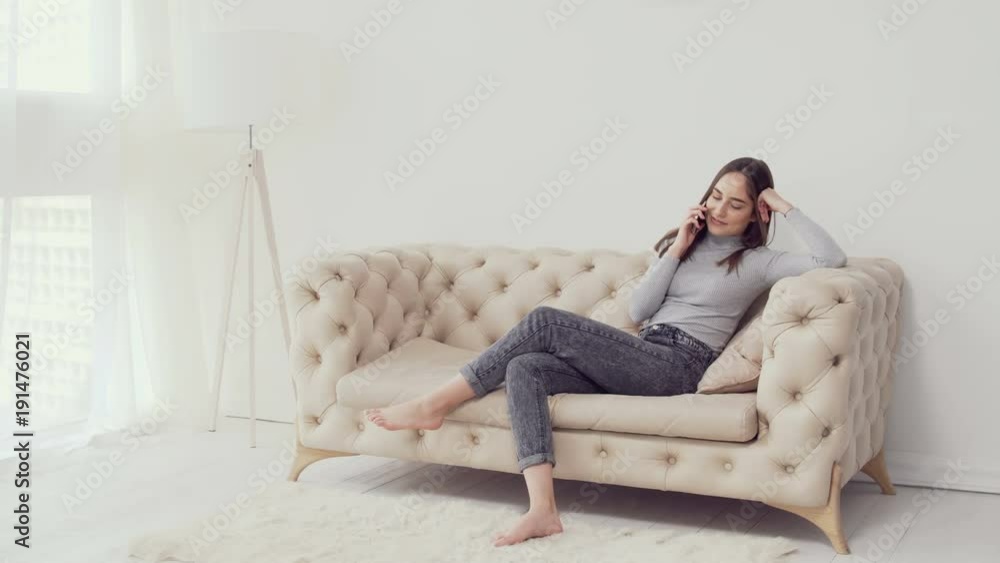 Young caucasian girl talking on the phone while sitting on sofa In white room. Young caucasian girl talking on the phone while sitting on sofa In white room.