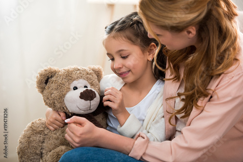 beautiful happy mother and daughter playing with teddy bear at home
