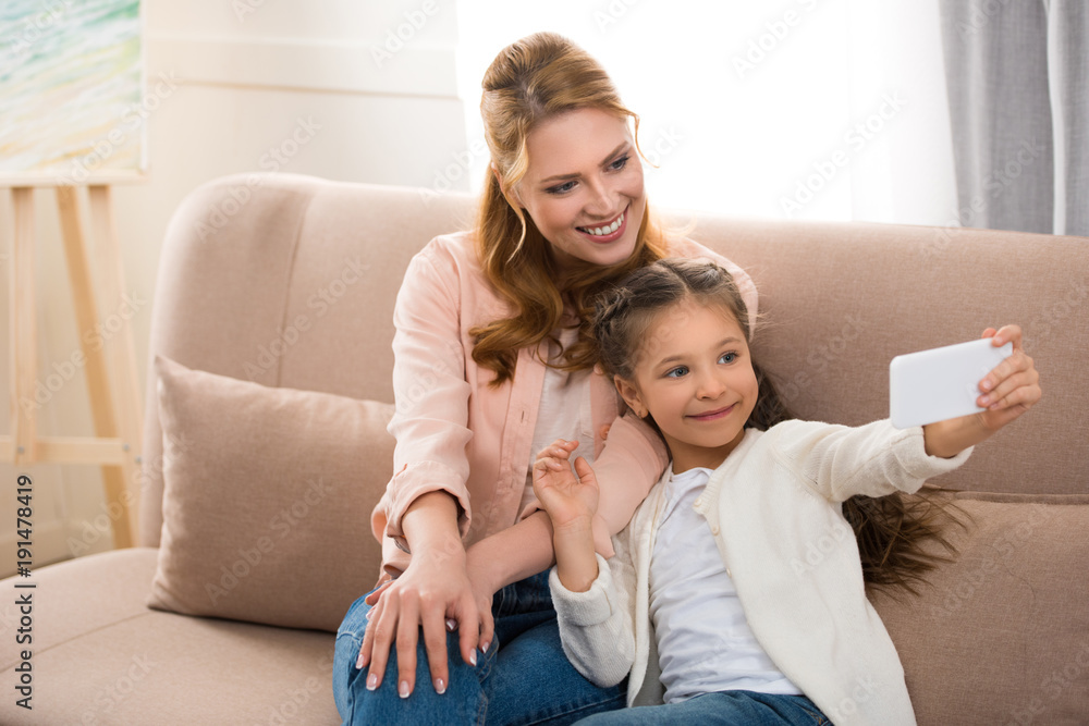 happy mother and daughter taking selfie with smartphone at home