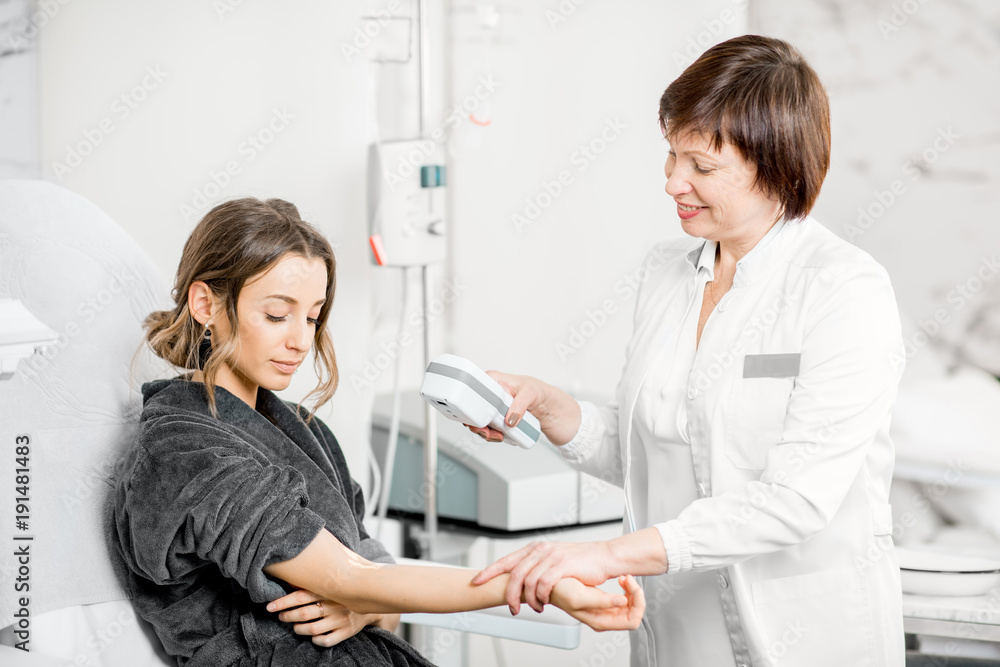 Fototapeta premium Senior doctor finding veins with vein scanner device to a young patient in a medical resort