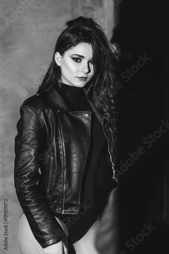 Portrait of a sexy girl with naked legs and in leather jacket posing in dark studio