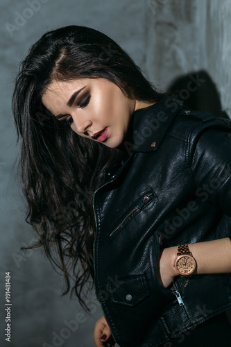 Portrait of a sexy girl with naked legs and in leather jacket posing in dark studio
