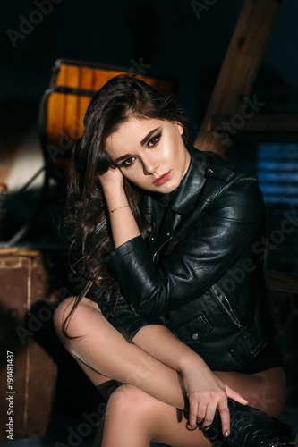 Portrait of a sexy girl with naked legs and in leather jacket posing in dark studio