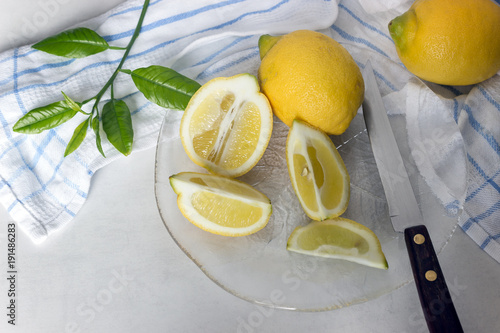 Juicy lemons and slices in transparent fancy dish. Nearby lies a knife and a kitchen towel.