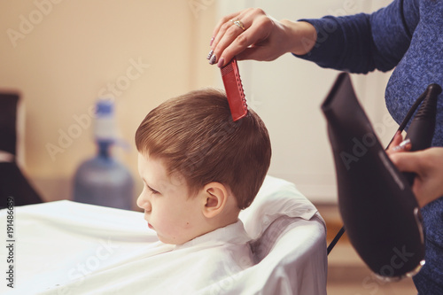 Hairdresser's hands making hairstyle to little boy, close up
