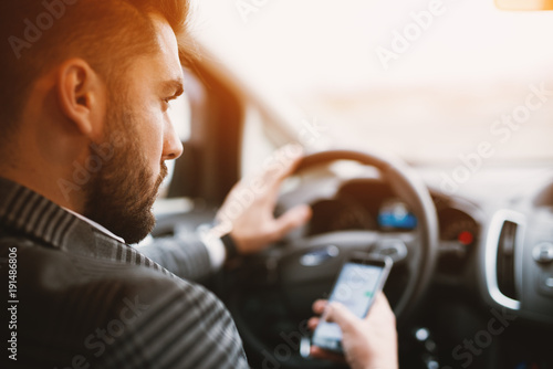 Attractive bearded man texting while driving an expencive car in a sunny weather. photo