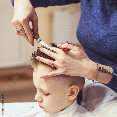 Little boy at the hairdresser. Child is scared of haircuts. Hairdresser's hands making hairstyle to little boy, close up © nata_zhekova