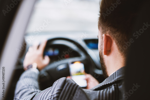 Rare view of a suited man checking phone while driving a car.