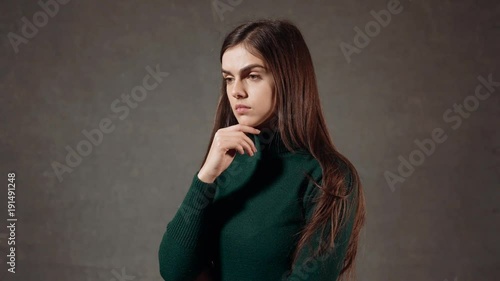 Portrait of a beautiful caucasian woman, wearing green turtleneck sweater, thinking seriously in the gray background