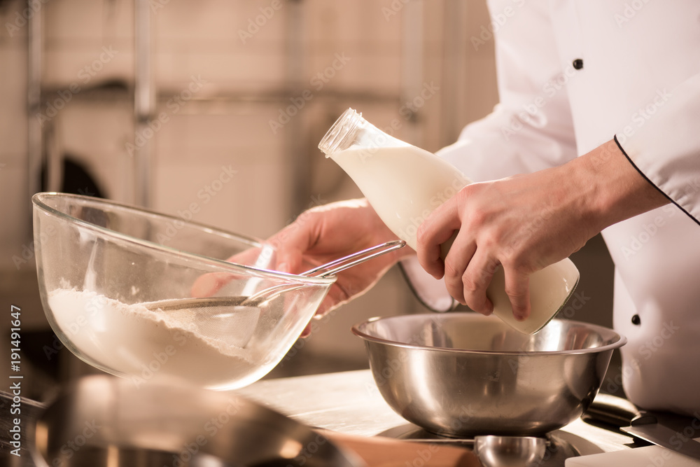 partial view of confectioner adding milk into dough in restaurant kitchen partial view of confectioner adding milk into dough in restaurant kitchen