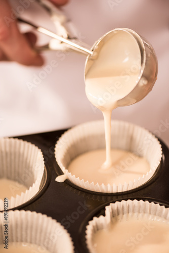cropped shot of confectioner pouring dough into baking forms