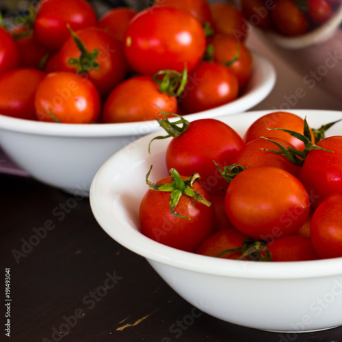 Whole cherry tomatoes in a white porcelain bowl on a brown wooden table