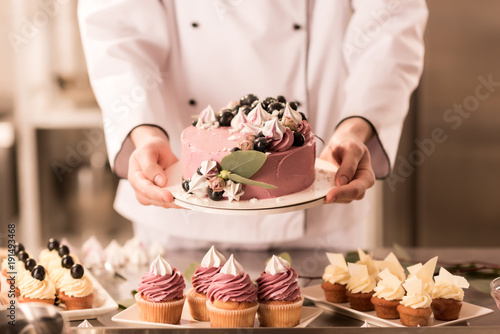 partial view of confectioner holding cake in hands in restaurant kitchen photo
