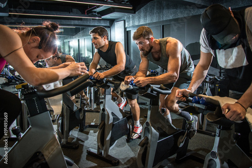 Sporty people riding stationary bicycles in gym.