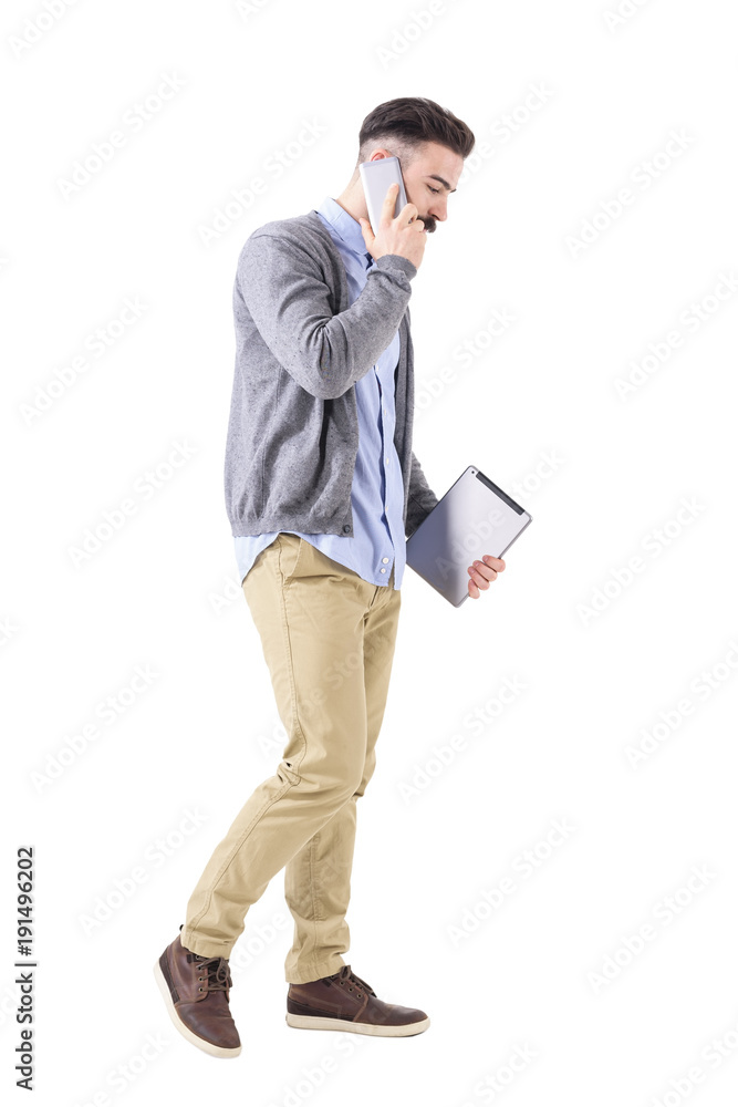 Business man talking on the phone walking and carrying tablet computer looking down. Full body length portrait isolated on white studio background. Business man talking on the phone walking and carrying tablet computer looking down. Full body length portrait isolated on white studio background.