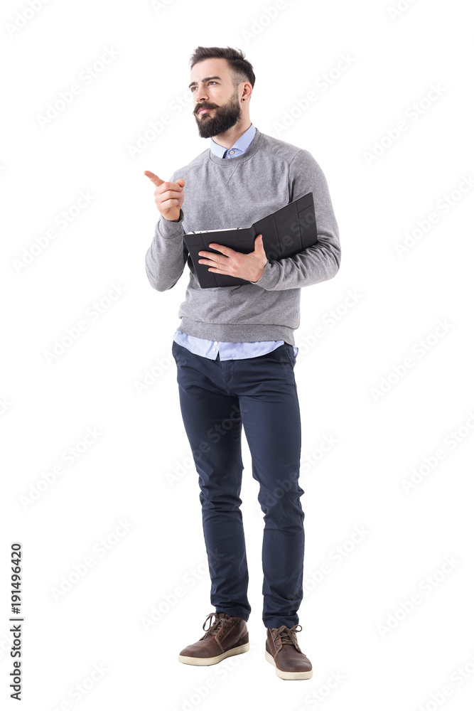Confident stylish bearded businessman holding notebook pointing and looking away. Full body length portrait isolated on white studio background. Confident stylish bearded businessman holding notebook pointing and looking away. Full body length portrait isolated on white studio background.