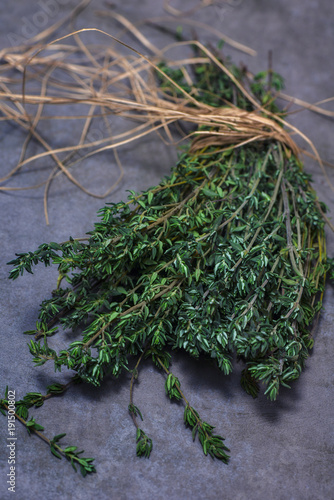 Bunch of thyme tied with straw rope on grey stone background.