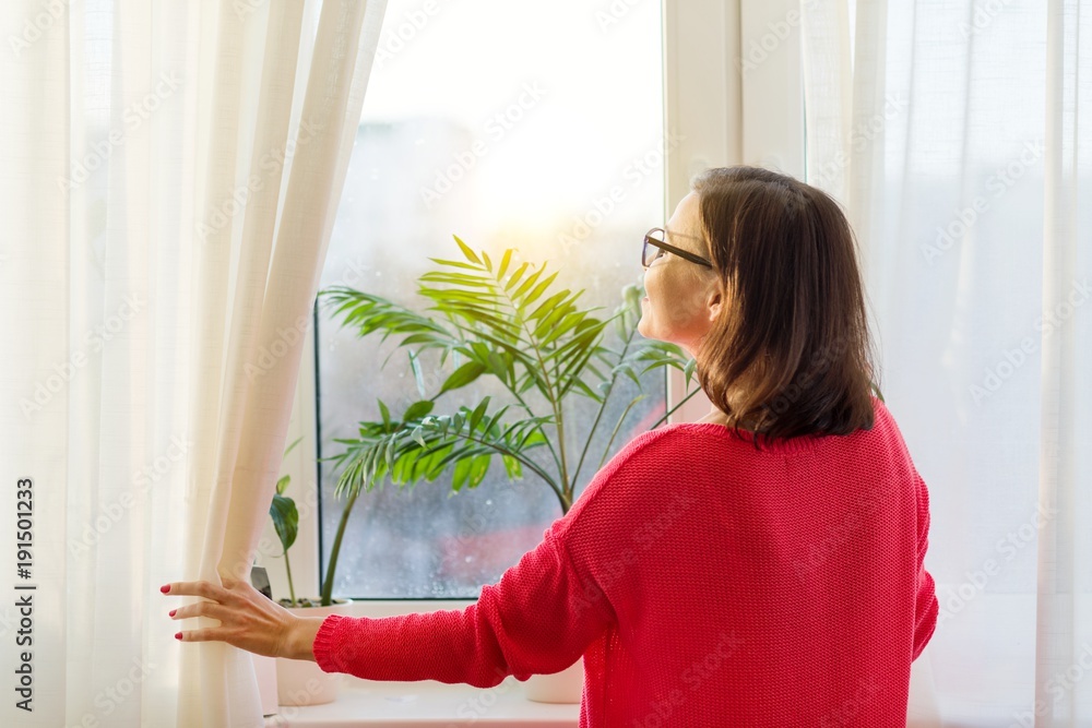 Woman looks out the window, opens the curtains. View from the back Woman looks out the window, opens the curtains. View from the back
