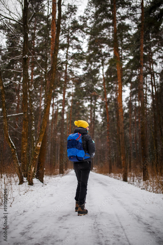 Photo from back of walking woman with backpack over winter forest