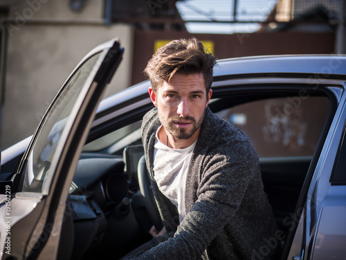 Portrait of attractive man in white shirt getting out of his new stylish polished car outdoor in city street © theartofphoto