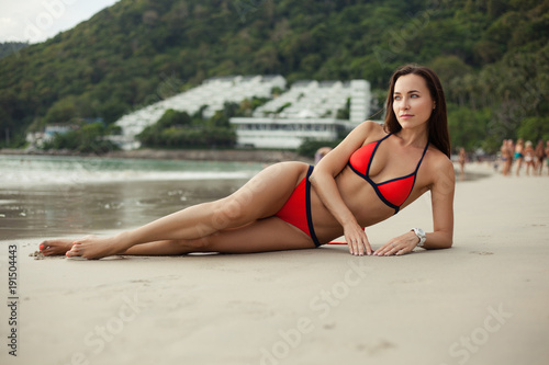 attractive young woman in red bikini resting on beach at the sea