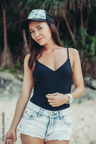 attractive girl in black bodysuit and cap posing at beach