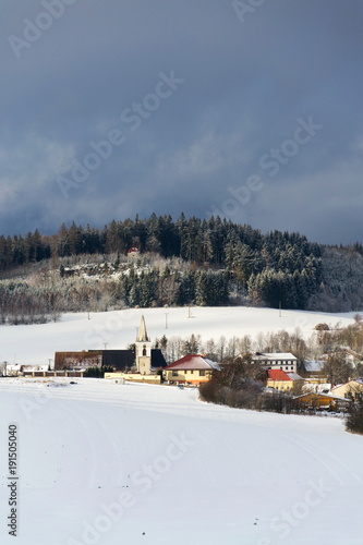 Catholic Church of the Birth of Virgin Mary in Milicin with Calvary on hill in snowy winter country in sunny day, Czech Republic