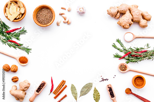 Colorful dry spices in bowls and spoons near ginger, garlic, rosemary, laurel leaf on white background top view copy space