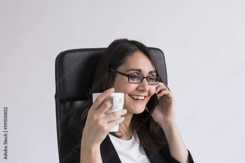 beautiful young Business woman talking on her mobile phone in the office and holding a cup of coffee. Business Concept. Lifestyle. Indoors beautiful young Business woman talking on her mobile phone in the office and holding a cup of coffee. Business Concept. Lifestyle. Indoors