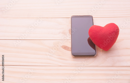 Red heart with smart phone on wooden table for valentine day concept.