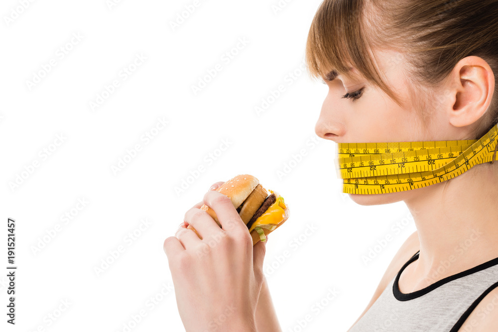 woman with mouth tied in measuring tape trying to eat burger isolated on white woman with mouth tied in measuring tape trying to eat burger isolated on white