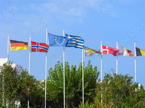 Flags of EU, Greece, Germany, Norway, Sweden, Denmark, France above green trees in blue sky. photo