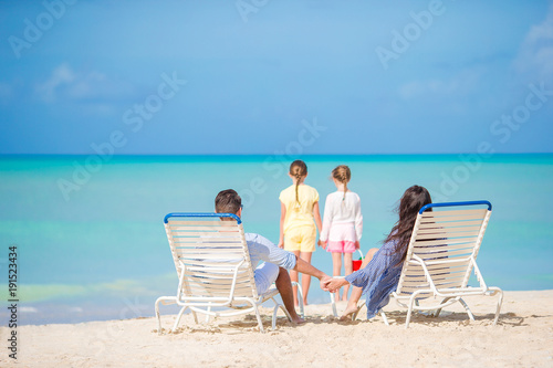 Fototapeta Naklejka Na Ścianę i Meble -  Happy beautiful family of four on the beach. Parents relaxing on sunbed and kids having fun on the coast