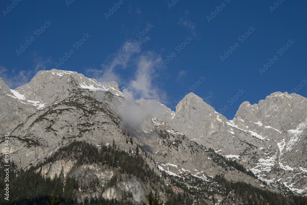 Dramatic alpine scenery with bare mountain peaks and coniferous forest in the foothills