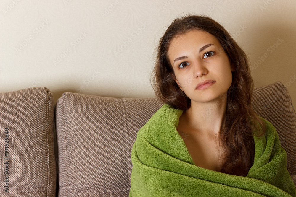 young woman feeling sick or sad wrapped in blanket and sitting on sofa. Teens psychological problems. medical and health concept young woman feeling sick or sad wrapped in blanket and sitting on sofa. Teens psychological problems. medical and health concept