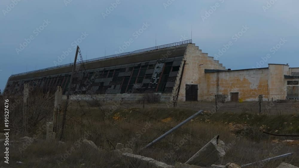 Abandoned military hangars and buildings in a closed area with barbed wire. Technical territory with technical objects. The camera moves slowly along the buildings. Abandoned military hangars and buildings in a closed area with barbed wire. Technical territory with technical objects. The camera moves slowly along the buildings.